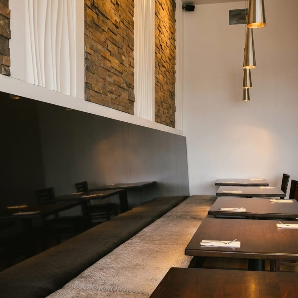 Modern restaurant interior with dark wooden tables, a long banquette, and stone accent walls.