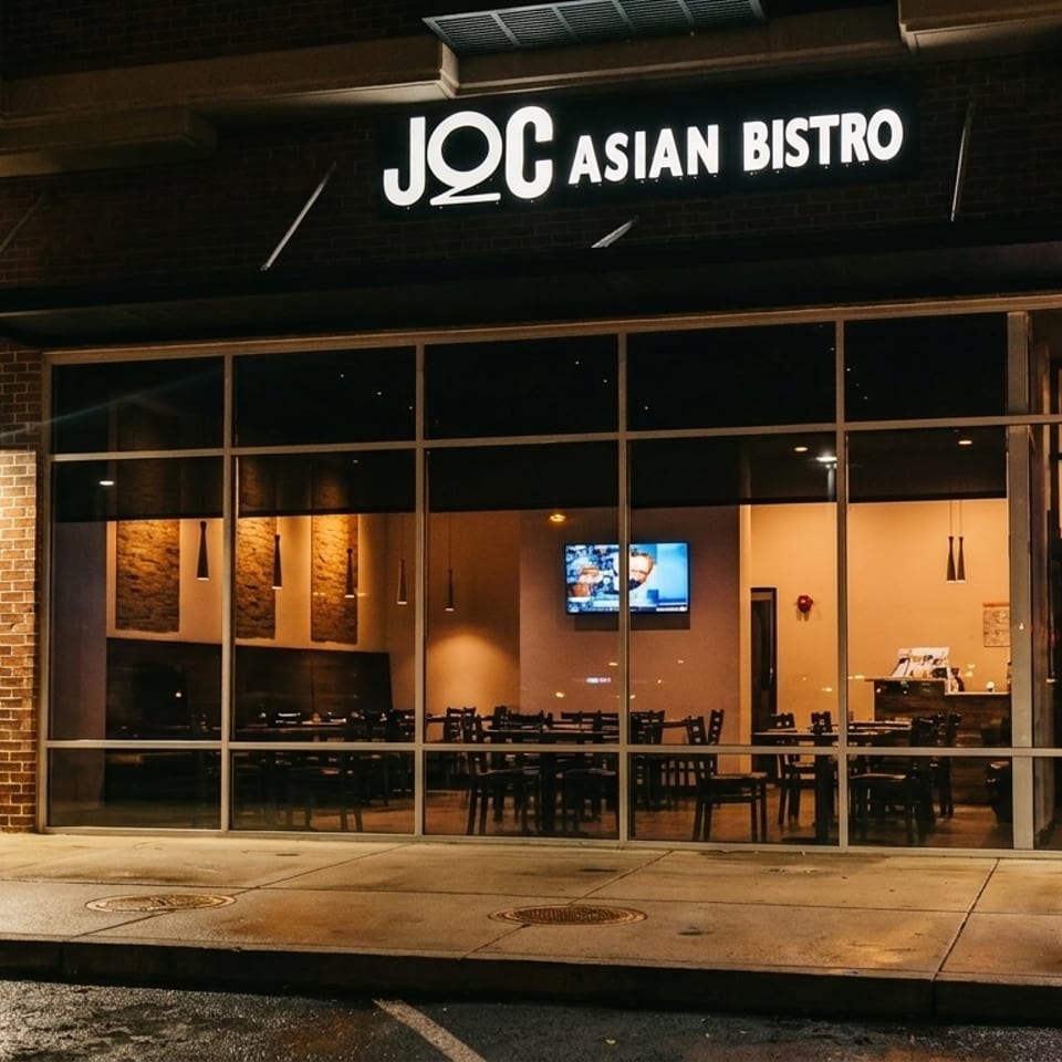 Exterior of JOC Asian Bistro at night, with an "OPEN" sign and visible dining room through large windows.